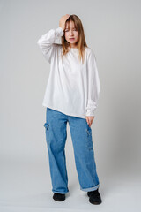 Young girl in a white sweater holding her head in discomfort against a minimalist background