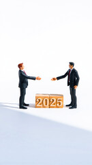 two miniature figures suits shake hands over a 2025 block