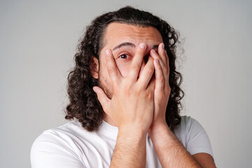 Young man covers his face with hands in a moment of surprise or shock against a neutral background