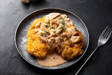 Fried chicken breast fillet in creamy mushroom sauce with champignons and oregano on the dark table