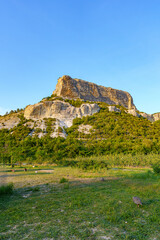 A rugged cliff rises above a green landscape under a clear blue sky