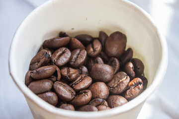 Coffee beans artistic shot in a white paper cup, brown bean, arabica and robusta, café, caffeine, white background, freshness, shot is selective focus with shallow depth of field, taken at Cairo Egypt