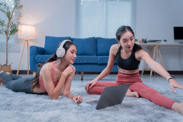 Naklejka premium Two young asian women are enjoying a relaxing yoga session in their living room, following an online class on their laptop and wearing headphones