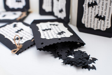 Naklejka premium Selbst gebastelte Halloween Dekoration zum Fest. Anhänger mit Totenkopf auf selbstgeschöpftem Papier und Konfetti in schwarz in Form von Kreuz und Fledermaus