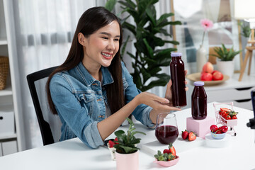 Smiling young beautiful Asian reviewing tasty mixed strawberry and cherry juice detox drinks, showing healthy product to promote for special promotion selling on social media online record. Stratagem.