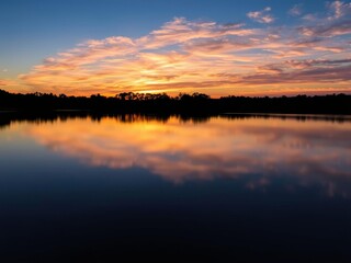 Obraz premium A serene landscape at dusk, with a silhouette of trees against a colorful sky reflecting on a smooth lake surface, sky, sunset