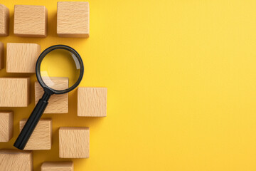 Magnifying glass on wooden blocks against bright yellow background