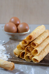 A stack of freshly baked Egg Roll cookies or biscuits displayed with flour and eggs, highlighting homemade baking with simple ingredients. Perfect for a cozy dessert or snack idea.