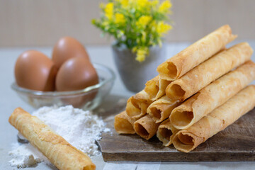 A stack of freshly baked Egg Roll cookies or biscuits displayed with flour and eggs, highlighting homemade baking with simple ingredients. Perfect for a cozy dessert or snack idea.