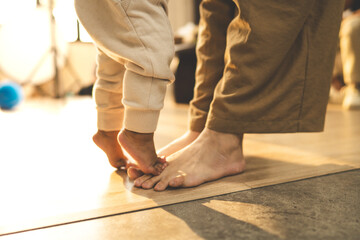 A close-up of a toddler standing on Mother's feet, capturing a warm moment of bonding, love, and...