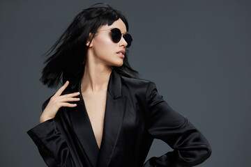 Beautiful asian woman in a black suit and sunglasses, posing confidently against a gray background