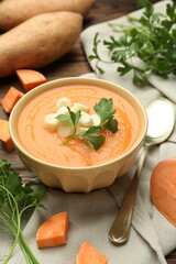 Delicious sweet potato soup with croutons in bowl, fresh vegetables and parsley on wooden table