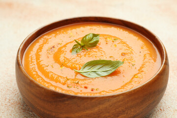 Delicious sweet potato soup with spices and basil in bowl on beige table, closeup