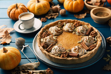 Homemade pumpkin pie with whipped cream, seeds and cinnamon on blue wooden table