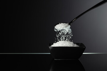 Sea salt in a small ceramic bowl on a black reflective background.
