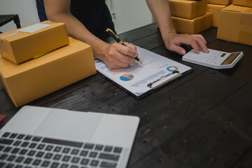 An Asian man carefully prepares a package for a customer's online order, methodically placing items in a box, sealing it securely, and attaching a shipping label for prompt delivery.