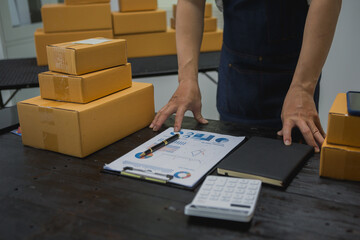 An Asian man carefully prepares a package for a customer's online order, methodically placing items...