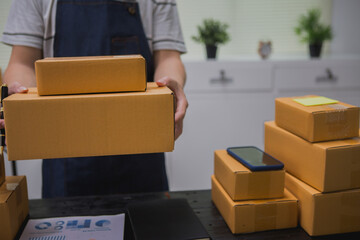 An Asian man carefully prepares a package for a customer's online order, methodically placing items in a box, sealing it securely, and attaching a shipping label for prompt delivery.