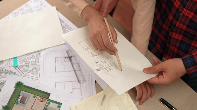 Smart architect and safety engineer discussion about building blueprint on table with architectural document, measurement tools and wooden block scatter around at modern office. Closeup. Delineation.