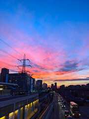 London, UK - 02.01.2024: Pink and golden evening glow over Custom House Elizabeth Line station alongside cars and a bus queuing before a red light 