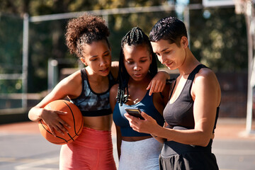 Basketball, friends and women with phone for sports schedule, social media or show results on chat app. Mobile, ball or group of girls outdoor on break after training, fitness or online game on court © peopleimages.com