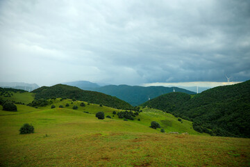 Obraz premium Serene Mountain Meadow with Distant Wind Turbines under Blue Sky 