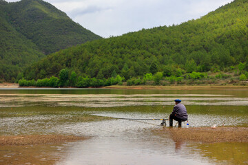 fishing man besede the lake near the mountain