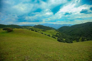 Obraz premium Serene Mountain Meadow with Distant Wind Turbines under Blue Sky 