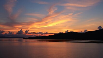 Fototapeta premium Vivid orange and pink sunset reflecting on calm water with silhouetted palm trees, colorful, landscape