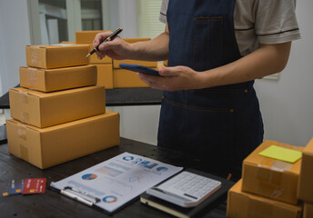 An Asian man carefully prepares a package for a customer's online order, methodically placing items in a box, sealing it securely, and attaching a shipping label for prompt delivery.