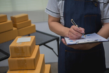 An Asian man carefully prepares a package for a customer's online order, methodically placing items in a box, sealing it securely, and attaching a shipping label for prompt delivery.