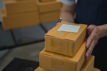 An Asian man carefully prepares a package for a customer's online order, methodically placing items...