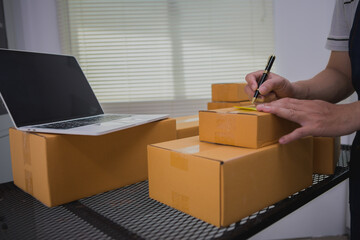 An Asian man carefully prepares a package for a customer's online order, methodically placing items...