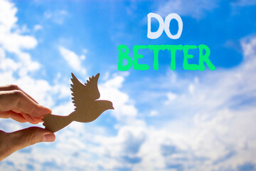 Do better symbol. Concept words Do better on beautiful blue sky. Beautiful blue sky clouds background. Hand holds wooden bird. Business and do better concept. Copy space.