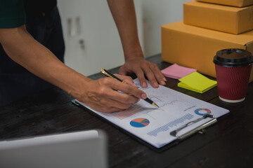 An Asian man carefully prepares a package for a customer's online order, methodically placing items in a box, sealing it securely, and attaching a shipping label for prompt delivery.