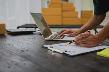 An Asian man carefully prepares a package for a customer's online order, methodically placing items in a box, sealing it securely, and attaching a shipping label for prompt delivery.