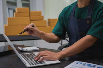 An Asian man carefully prepares a package for a customer's online order, methodically placing items in a box, sealing it securely, and attaching a shipping label for prompt delivery.