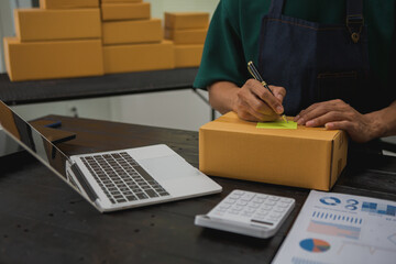 An Asian man carefully prepares a package for a customer's online order, methodically placing items in a box, sealing it securely, and attaching a shipping label for prompt delivery.