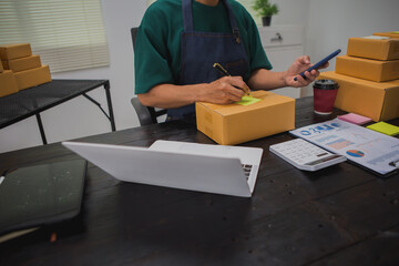 An Asian man carefully prepares a package for a customer's online order, methodically placing items in a box, sealing it securely, and attaching a shipping label for prompt delivery.