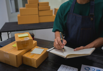 An Asian man carefully prepares a package for a customer's online order, methodically placing items in a box, sealing it securely, and attaching a shipping label for prompt delivery.