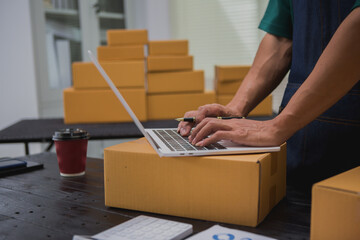 An Asian man carefully prepares a package for a customer's online order, methodically placing items...