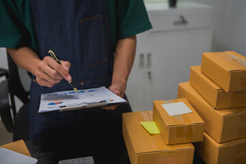 An Asian man carefully prepares a package for a customer's online order, methodically placing items in a box, sealing it securely, and attaching a shipping label for prompt delivery.