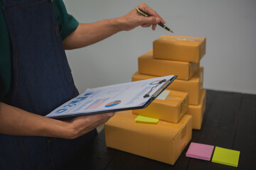 An Asian man carefully prepares a package for a customer's online order, methodically placing items in a box, sealing it securely, and attaching a shipping label for prompt delivery.
