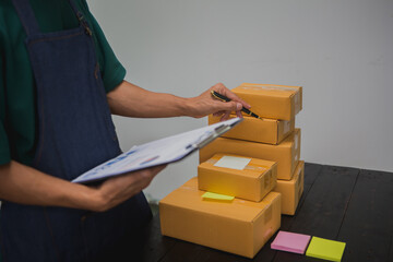 An Asian man carefully prepares a package for a customer's online order, methodically placing items in a box, sealing it securely, and attaching a shipping label for prompt delivery.