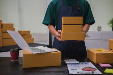 An Asian man carefully prepares a package for a customer's online order, methodically placing items in a box, sealing it securely, and attaching a shipping label for prompt delivery.