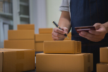 An Asian man carefully prepares a package for a customer's online order, methodically placing items...