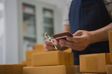An Asian man carefully prepares a package for a customer's online order, methodically placing items...