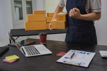 An Asian man carefully prepares a package for a customer's online order, methodically placing items...