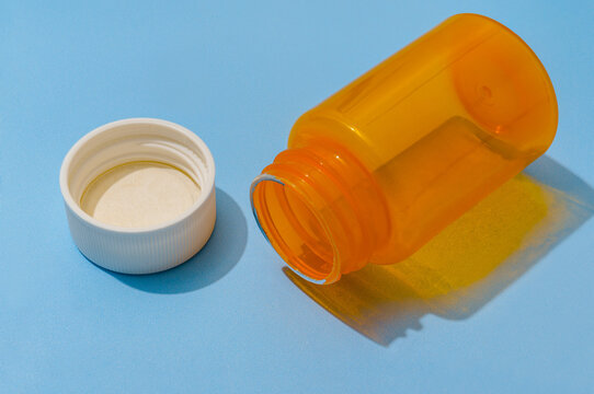Empty Orange Pill Bottle and White Cap on Blue Background