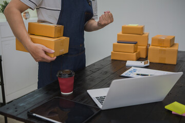 An Asian man carefully prepares a package for a customer's online order, methodically placing items...